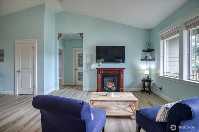 566 Duck Lake Dr SE, Ocean Shores, WA 98569 - living area featuring light wood-style flooring, lofted ceiling, a glass covered fireplace, and baseboards