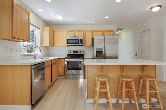 3147 6th Ave NW, Olympia, WA 98502 - kitchen with appliances with stainless steel finishes, a sink, light wood-style flooring, a kitchen breakfast bar, and recessed lighting