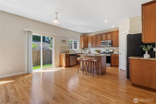 27677 256th Pl SE, Maple Valley, WA 98038 - kitchen featuring appliances with stainless steel finishes, brown cabinetry, a breakfast bar, tasteful backsplash, and a center island