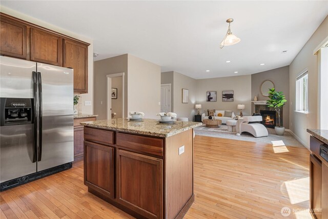 27677 256th Pl SE, Maple Valley, WA 98038 - kitchen featuring stainless steel fridge, light wood-style flooring, a glass covered fireplace, a kitchen island, and open floor plan