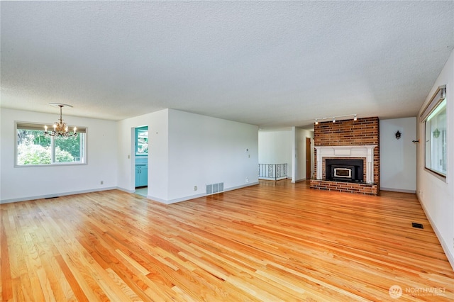434 T St, Port Townsend, WA 98368 - unfurnished living room with a textured ceiling, light wood-style flooring, a chandelier, a brick fireplace, and baseboards