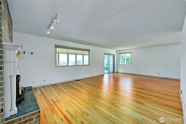434 T St, Port Townsend, WA 98368 - unfurnished living room featuring a textured ceiling, rail lighting, wood finished floors, a wood stove, and baseboards