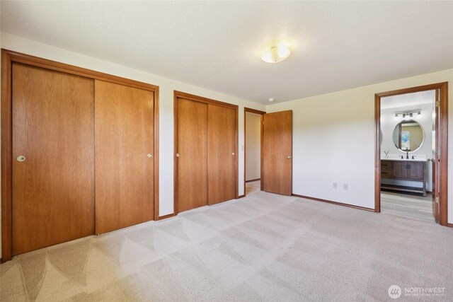 13820 Logez Ct SW, Olympia, WA 98512 - unfurnished bedroom with multiple closets, light carpet, baseboards, ensuite bath, and a sink