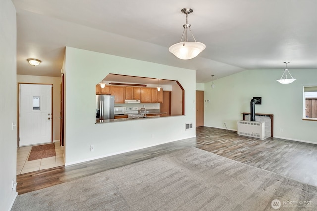 546 Canal Dr NE, Ocean Shores, WA 98569 - unfurnished living room featuring wood finished floors, a wood stove, vaulted ceiling, radiator heating unit, and arched walkways
