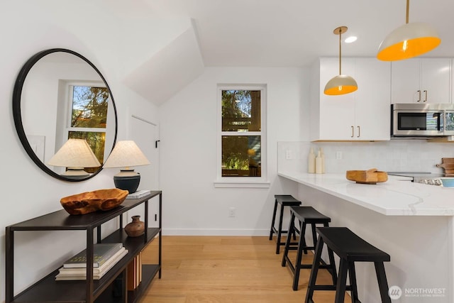 5613 43rd Ave NE, Seattle, WA 98105 - kitchen with stainless steel microwave, white cabinetry, light wood-style floors, backsplash, and decorative light fixtures