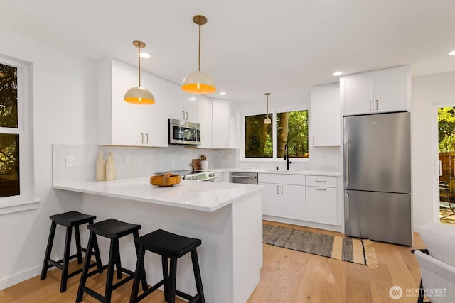 5613 43rd Ave NE, Seattle, WA 98105 - kitchen with appliances with stainless steel finishes, a sink, a peninsula, light wood-type flooring, and decorative backsplash
