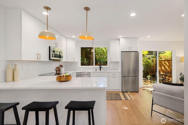 5613 43rd Ave NE, Seattle, WA 98105 - kitchen featuring appliances with stainless steel finishes, a peninsula, a sink, light wood-style floors, and white cabinets