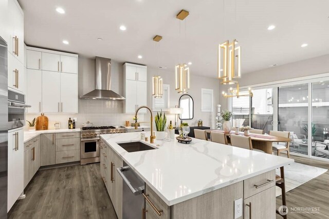 215 8th Ave W, Kirkland, WA 98033 - kitchen featuring wall chimney exhaust hood, appliances with stainless steel finishes, a sink, dark wood-style floors, and a center island with sink