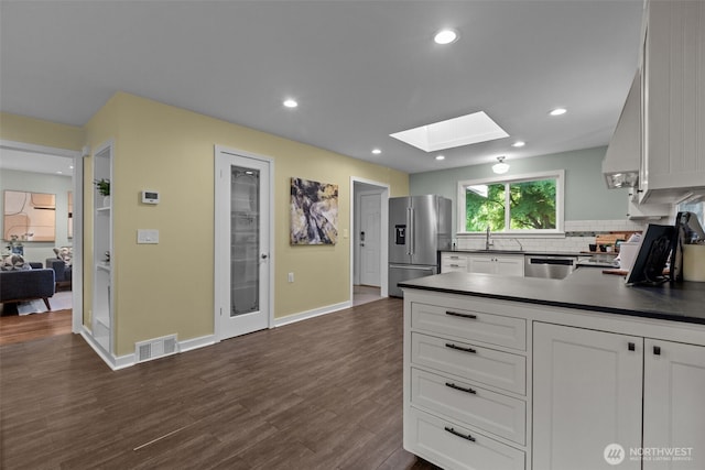 1716 N 125th St, Seattle, WA 98133 - kitchen with appliances with stainless steel finishes, dark countertops, a skylight, white cabinetry, and backsplash