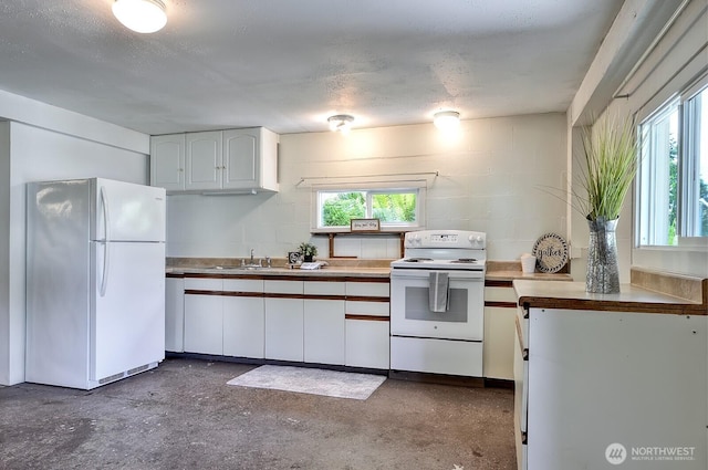 1160 St Paul St, Bellingham, WA 98229 - kitchen featuring white appliances, white cabinetry, healthy amount of natural light, and concrete block wall