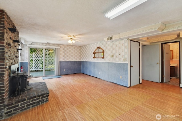 32427 6th Ave, Black Diamond, WA 98010 - unfurnished living room featuring wallpapered walls, a wood stove, a textured ceiling, wood finished floors, and a wainscoted wall