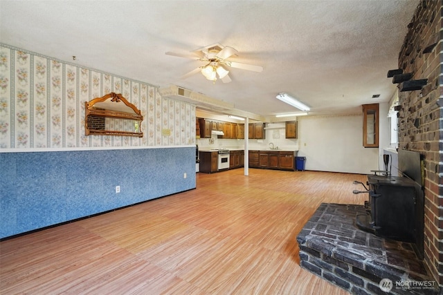 32427 6th Ave, Black Diamond, WA 98010 - living room featuring a wood stove, wallpapered walls, light wood-style flooring, a ceiling fan, and wainscoting