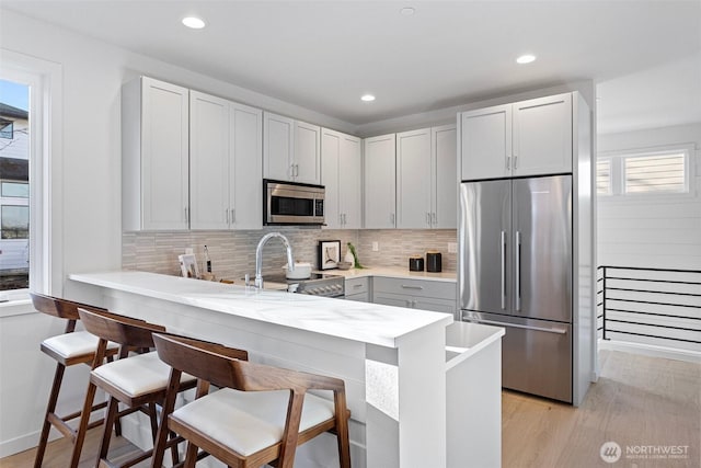8017 126th Ave NE Unit B, Kirkland, WA 98033 - kitchen with appliances with stainless steel finishes, backsplash, a peninsula, a breakfast bar, and light wood-style flooring