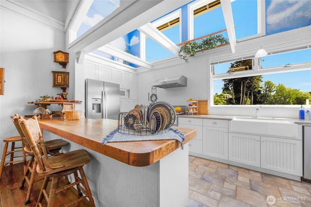 17257 Olympic View Rd NW, Silverdale, WA 98383 - kitchen featuring stainless steel refrigerator with ice dispenser, a kitchen bar, light stone finish floors, white cabinetry, and extractor fan