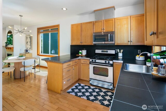 1414 25th Ave Unit B, Seattle, WA 98122 - kitchen with appliances with stainless steel finishes, a peninsula, decorative backsplash, a chandelier, and light wood-type flooring