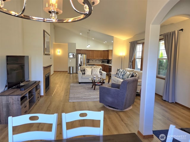 10127 Terra Valley St SE, Yelm, WA 98597 - living room featuring a chandelier, light wood-style floors, arched walkways, a fireplace with flush hearth, and lofted ceiling