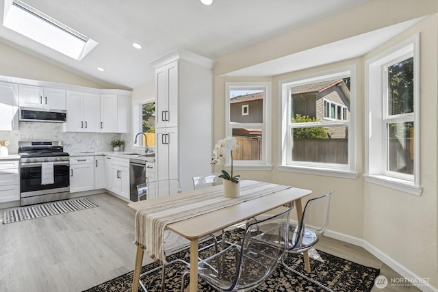 16828 Ambaum Blvd S, Burien, WA 98148 - kitchen featuring stainless steel appliances, vaulted ceiling, white cabinets, light wood-style floors, and a skylight