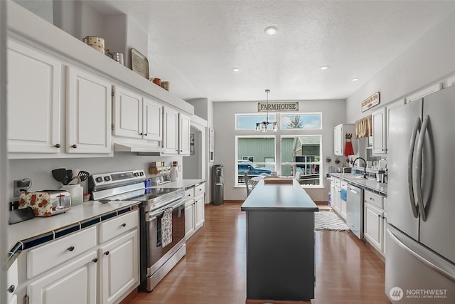 10419 Sandridge Rd, Long Beach, WA 98631 - kitchen with stainless steel appliances, a kitchen island, under cabinet range hood, white cabinetry, and wood finished floors