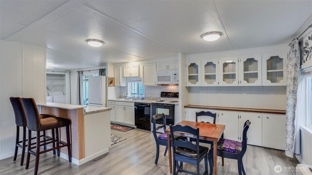 1510 Maple Ln Unit 16, Kent, WA 98030 - kitchen featuring white appliances, washing machine and clothes dryer, light wood-type flooring, white cabinets, and a breakfast bar area
