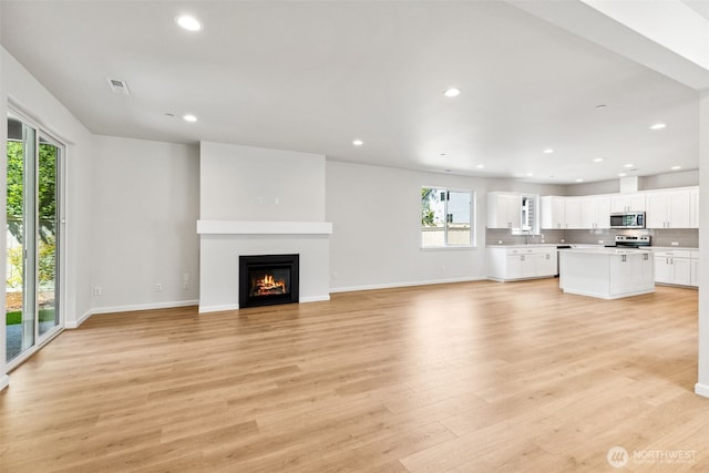 16617 8th Avenue Ct E Unit 9, Spanaway, WA 98387 - unfurnished living room with healthy amount of natural light, recessed lighting, light wood finished floors, and a glass covered fireplace