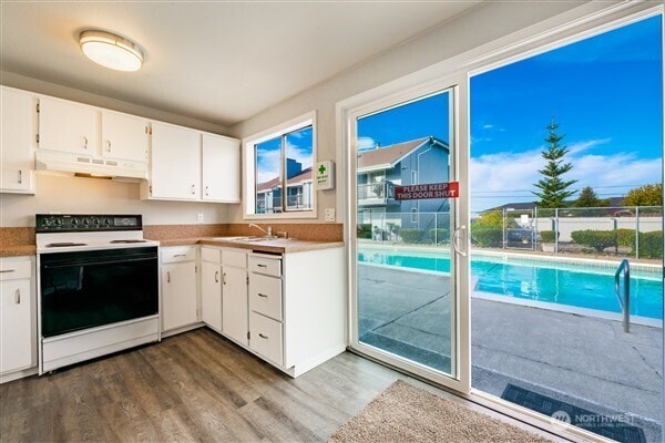 7530 Birch Bay Dr Unit 206, Blaine, WA 98230 - kitchen with electric range, under cabinet range hood, dark wood finished floors, white cabinetry, and a sink