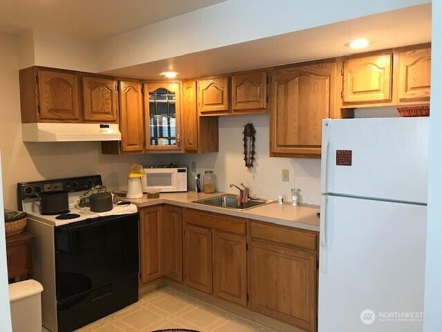 2513 13th Ave W, Seattle, WA 98119 - kitchen with white appliances, extractor fan, brown cabinetry, light countertops, and glass insert cabinets