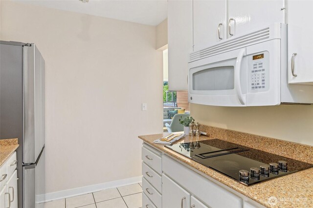 101 NW 58th St Unit 9, Seattle, WA 98107 - kitchen with freestanding refrigerator, white microwave, black electric cooktop, light tile patterned flooring, and white cabinetry