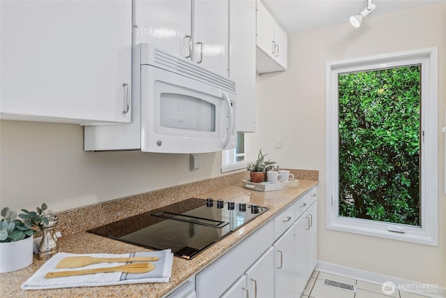 101 NW 58th St Unit 9, Seattle, WA 98107 - kitchen featuring white microwave, black electric stovetop, white cabinetry, and light tile patterned flooring