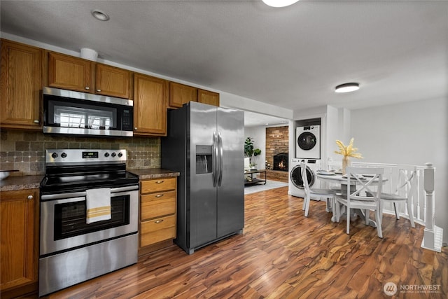1315 SW 310th St, Federal Way, WA 98023 - kitchen with stainless steel appliances, stacked washer / drying machine, brown cabinetry, and backsplash