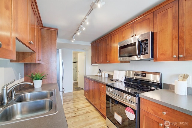 919 2nd Ave W Unit 601, Seattle, WA 98119 - kitchen with appliances with stainless steel finishes, a sink, brown cabinets, light wood-type flooring, and rail lighting