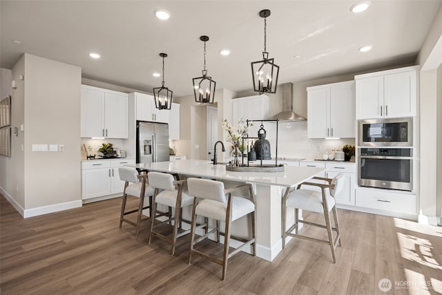 13920 181st St E Unit 64, Puyallup, WA 98374 - kitchen featuring stainless steel appliances, wall chimney range hood, light wood finished floors, a center island with sink, and recessed lighting