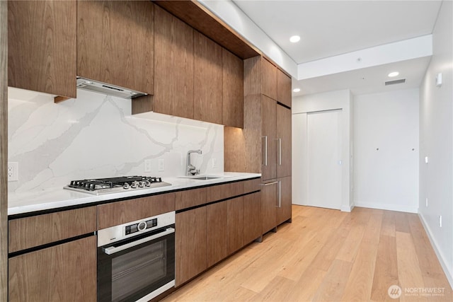 121 Stewart St Unit 3004, Seattle, WA 98101 - kitchen featuring stainless steel appliances, a sink, under cabinet range hood, backsplash, and light countertops