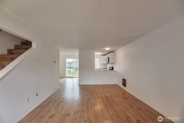 1702 C St SE, Auburn, WA 98002 - unfurnished living room featuring a textured ceiling, light wood-type flooring, stairs, and baseboards