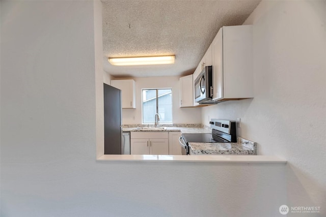 1702 C St SE, Auburn, WA 98002 - kitchen featuring appliances with stainless steel finishes, a sink, light countertops, white cabinetry, and a textured ceiling