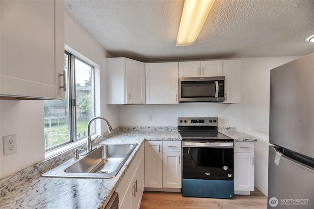 1702 C St SE, Auburn, WA 98002 - kitchen with appliances with stainless steel finishes, a sink, light wood-style flooring, a textured ceiling, and plenty of natural light