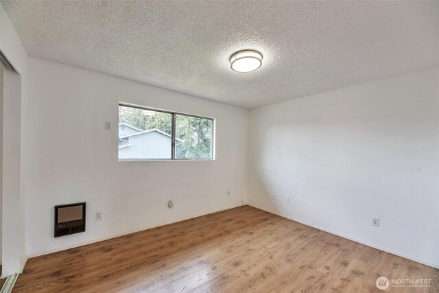 1702 C St SE, Auburn, WA 98002 - unfurnished room featuring a textured ceiling, wood finished floors, and heating unit