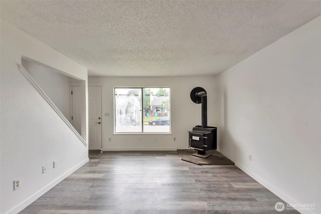 1702 C St SE, Auburn, WA 98002 - unfurnished living room featuring a textured ceiling, a wood stove, wood finished floors, and baseboards