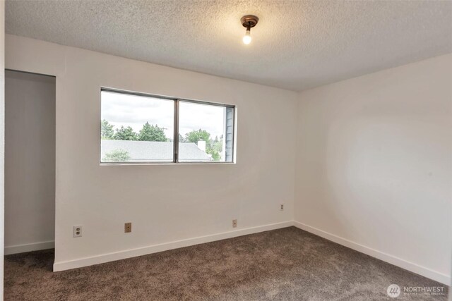 1702 C St SE, Auburn, WA 98002 - empty room featuring a textured ceiling, dark colored carpet, and baseboards