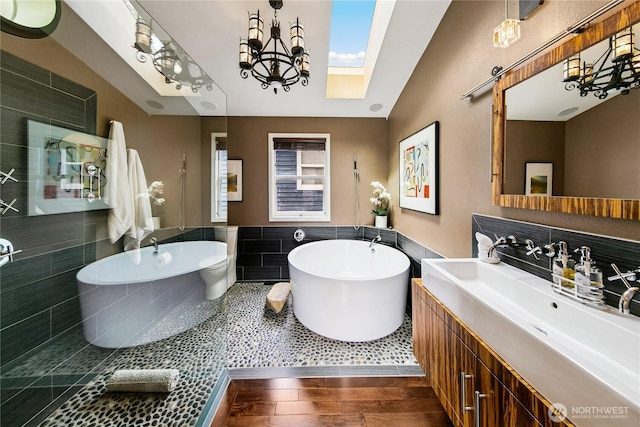 444 26th Ave E, Seattle, WA 98112 - full bathroom featuring tile walls, vanity, a freestanding tub, a skylight, and wood finished floors