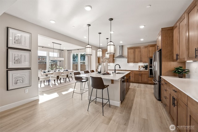 13912 181st St E Unit 62, Puyallup, WA 98374 - kitchen featuring wall chimney exhaust hood, brown cabinetry, appliances with stainless steel finishes, a breakfast bar area, and a center island with sink