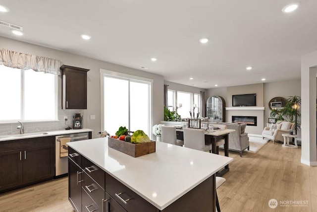 3905 98th Avenue Ct E Unit 33, Edgewood, WA 98371 - kitchen with stainless steel dishwasher, a glass covered fireplace, light countertops, dark brown cabinetry, and light wood-style flooring