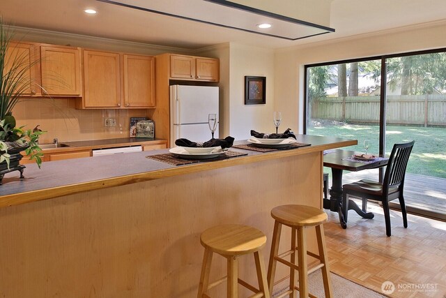 311 Edgecliff Dr, Langley, WA 98260 - kitchen with white appliances, light brown cabinetry, a kitchen bar, decorative backsplash, and ornamental molding
