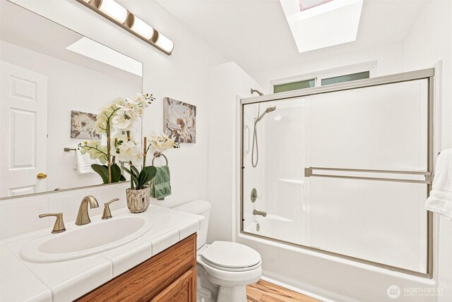 8471 E Caraway Rd, Port Orchard, WA 98366 - bathroom featuring toilet, vanity, a skylight, bath / shower combo with glass door, and wood finished floors