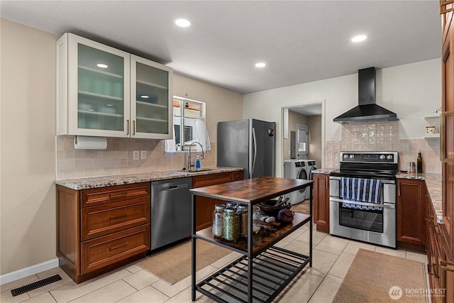 1011 Idaho St, Wenatchee, WA 98801 - kitchen featuring stainless steel appliances, wall chimney range hood, washer and clothes dryer, a sink, and decorative backsplash