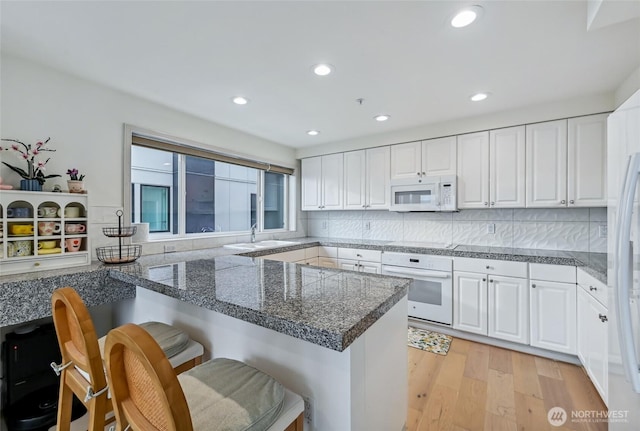 601 W Mercer Pl Unit 201, Seattle, WA 98119 - kitchen featuring white appliances, a kitchen breakfast bar, white cabinetry, and recessed lighting