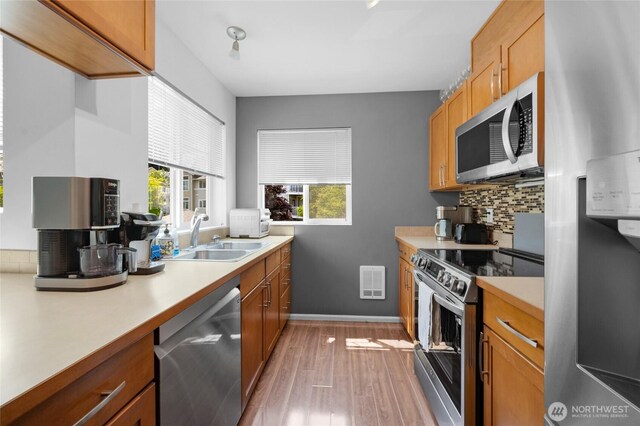21230 40th Way S Unit D, Seatac, WA 98198 - kitchen featuring appliances with stainless steel finishes, a sink, light wood-style floors, light countertops, and decorative backsplash