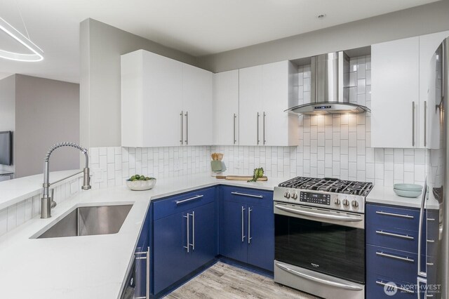 124 Bellevue Ave E Unit 305, Seattle, WA 98102 - kitchen with wall chimney range hood, stainless steel range with gas stovetop, a sink, light countertops, and blue cabinetry