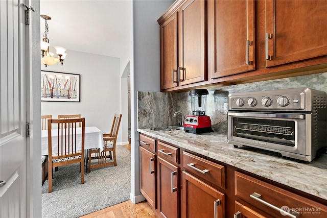 8521 15th Ave SE, Olympia, WA 98513 - kitchen with decorative backsplash, light stone countertops, brown cabinetry, a chandelier, and light wood-style flooring