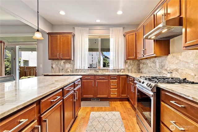 8521 15th Ave SE, Olympia, WA 98513 - kitchen with stainless steel gas stove, under cabinet range hood, light wood-style floors, decorative light fixtures, and light stone countertops