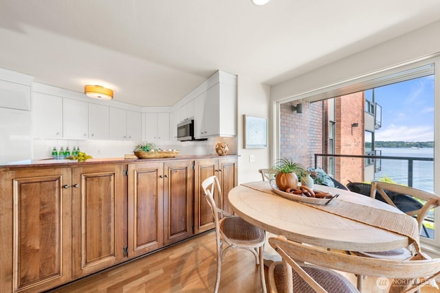 2360 43rd Ave E Unit 213, Seattle, WA 98112 - kitchen with light wood-style flooring, stainless steel microwave, brown cabinetry, a water view, and white cabinets